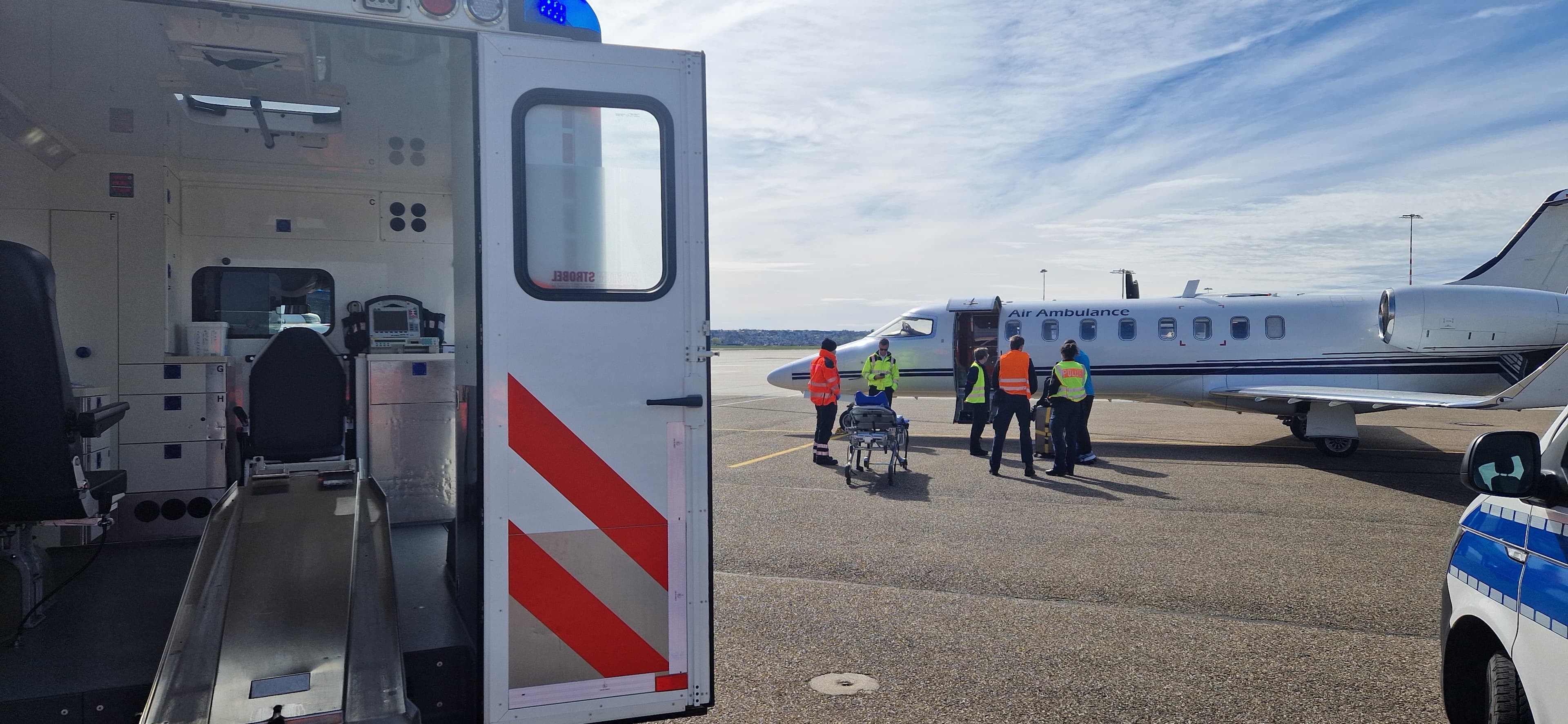Medical crew with a stretcher stand beside an air ambulance plane on a sunny tarmac.