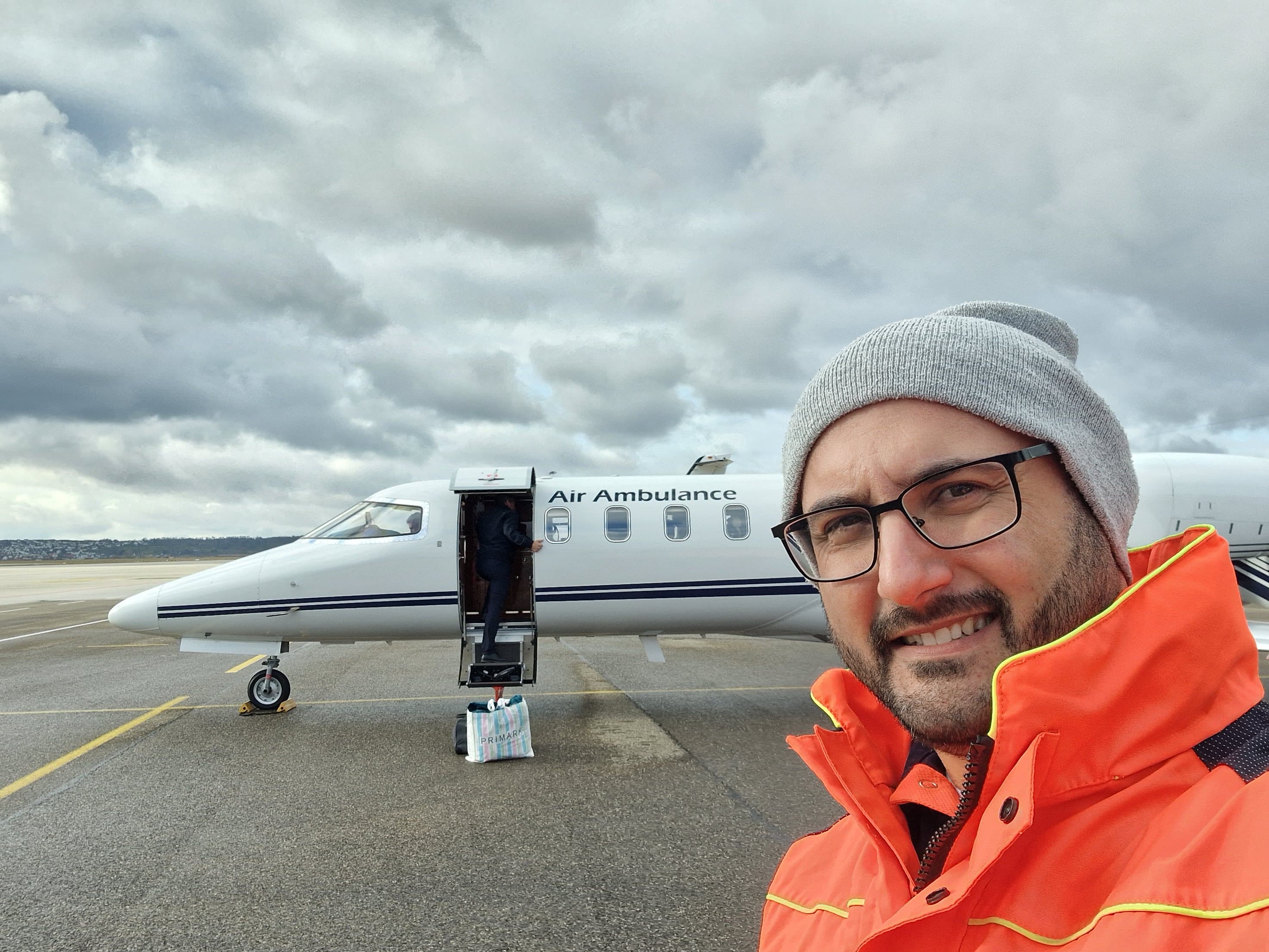 Man in orange jacket taking a selfie in front of a white air ambulance.