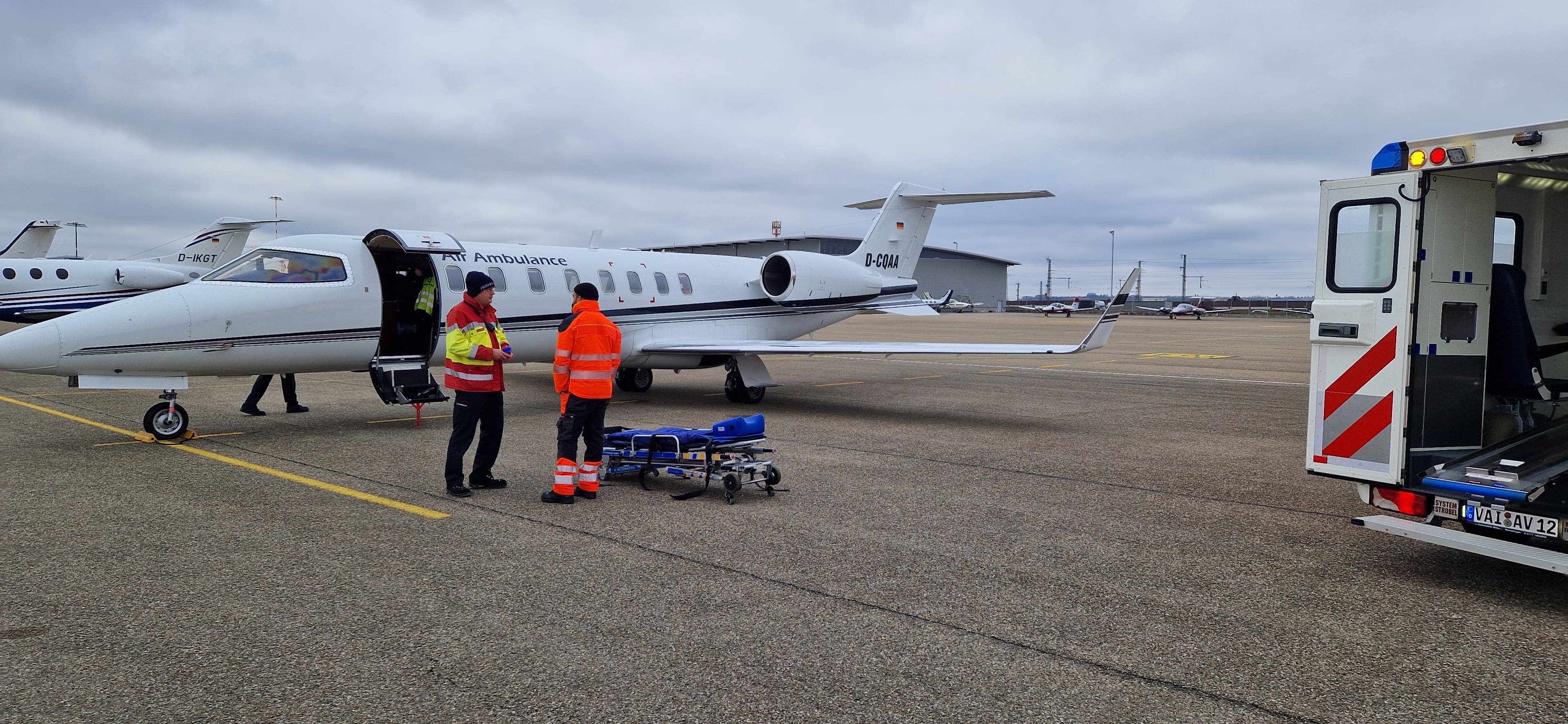 Two medical personnel with a stretcher stand beside an air ambulance jet on a tarmac.