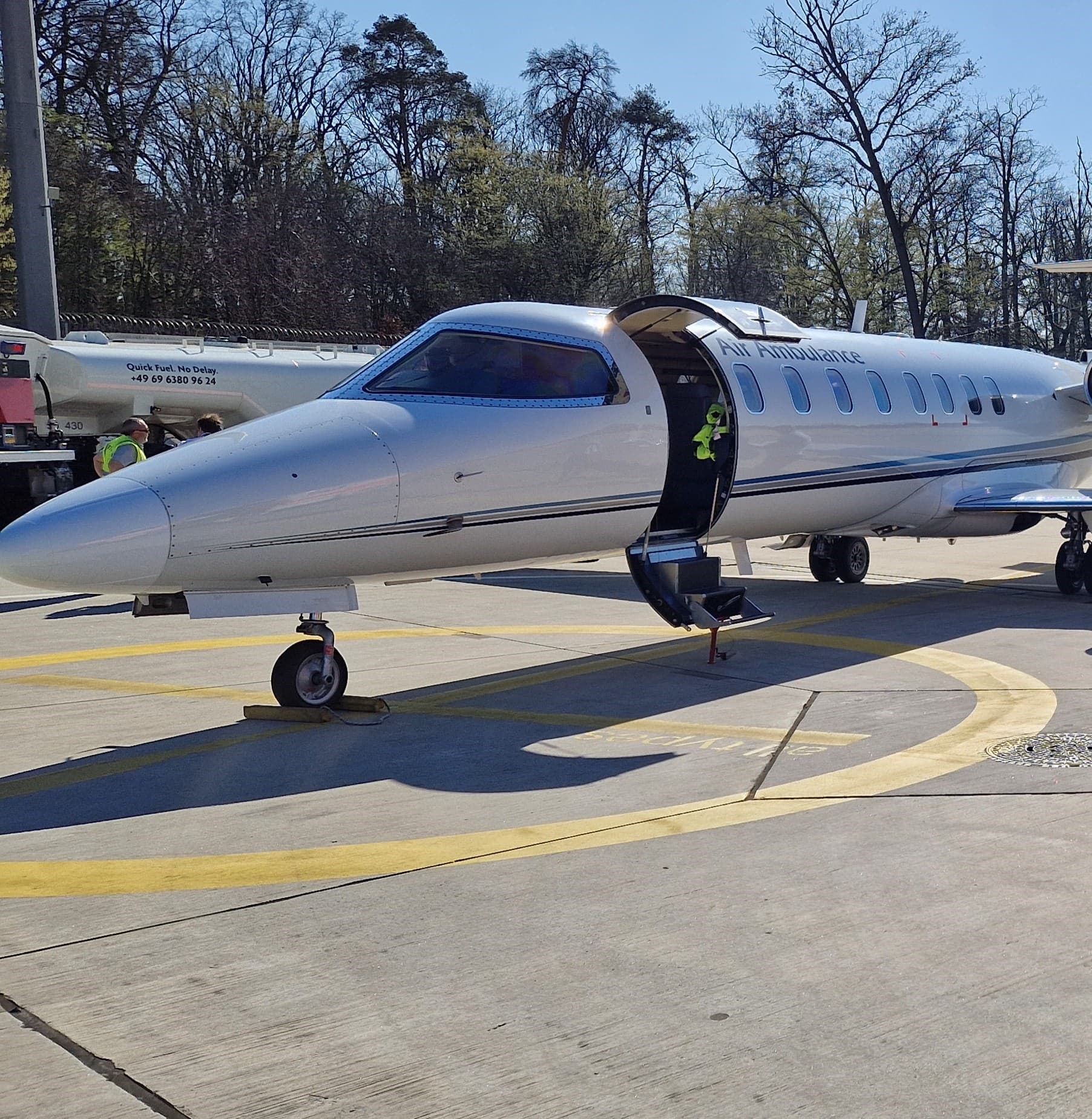 White air ambulance jet parked on a sunny airport tarmac with its cabin door open.